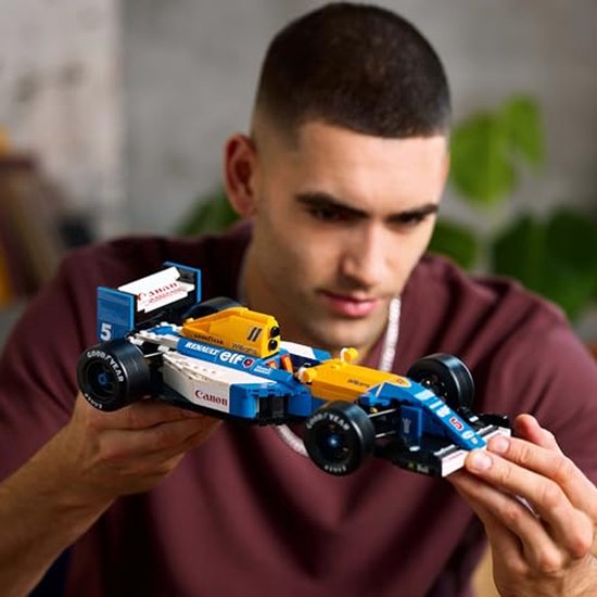 Een man houdt een Lego Williams Formule 1 auto, met gele en blauwe kleuren.