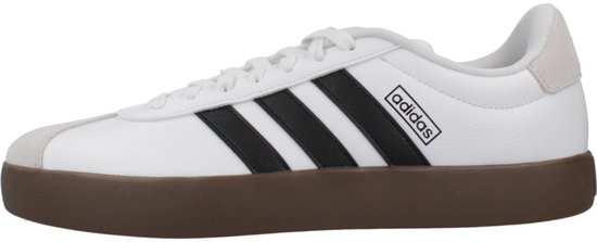 Zijaanzicht van een witte Adidas sneaker met zwarte strepen, grijze suède accenten en bruine zool.