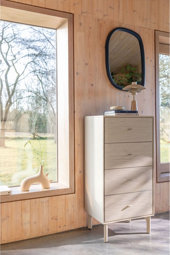 Beige ladekast met 4 geribbelde lades in een houten kamer met een spiegel en decoratie.
