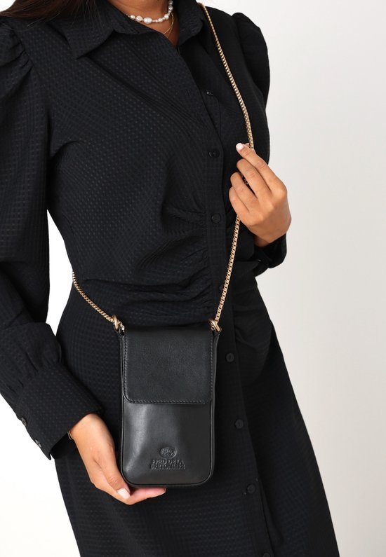 Vrouw met zwarte jurk draagt zwarte Fred de la Bretoniere telefoontas met gouden ketting.