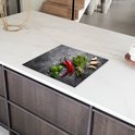 Inductiebeschermer met betonprint, versierd met rode pepers, knoflook en kruiden, op een wit aanrecht.