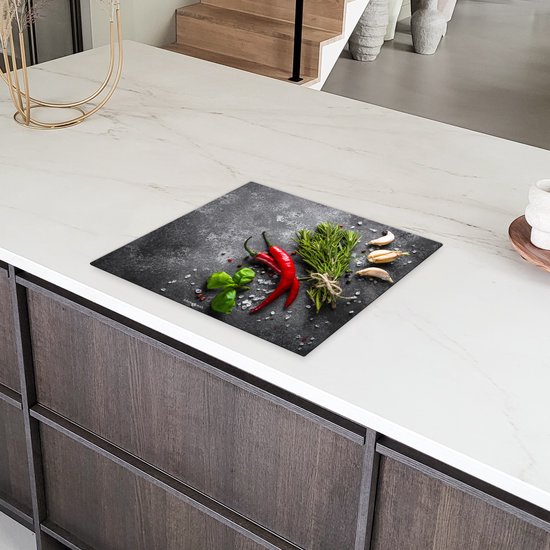 Inductiebeschermer met betonprint, versierd met rode pepers, knoflook en kruiden, op een wit aanrecht.
