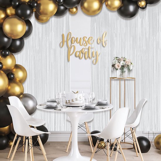 Feestversiering met ballonnen, een witte tafel met gebak, bloemen en 'House of Party' tekst, tegen een wit foliegordijn.