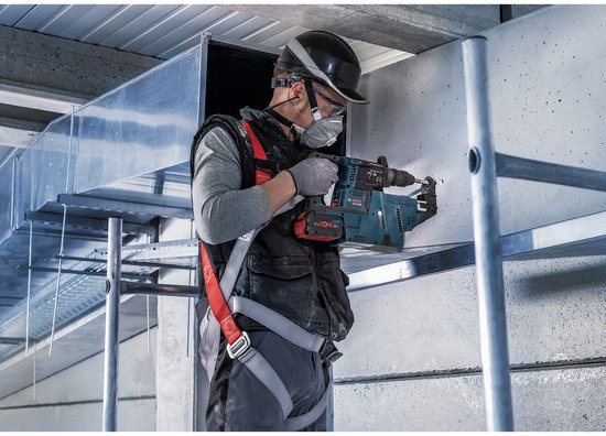 Man met helm, veiligheidsbril en mondkapje gebruikt een Bosch boorhamer aan een betonnen muur.