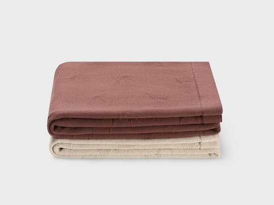 Twee gevouwen dekens; een donkerroze met een subtiel maanpatroon en een beige met een ruitpatroon.