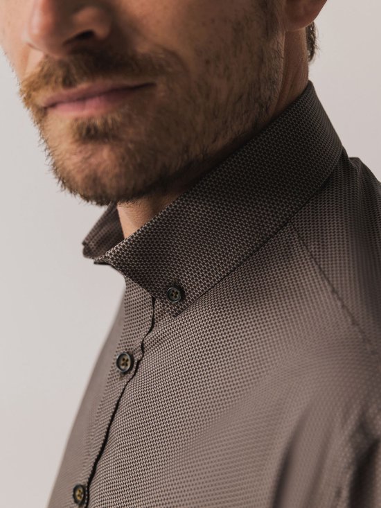 Close-up van een man met bruin overhemd met print, focus op kraag en knopen.
