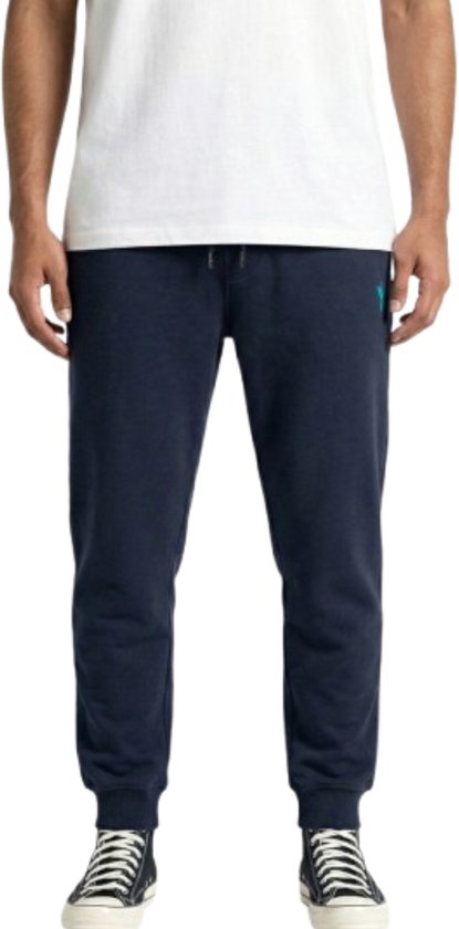 Navy joggingbroek met petrolblauw logo op de linkerheup, gedragen door een model.