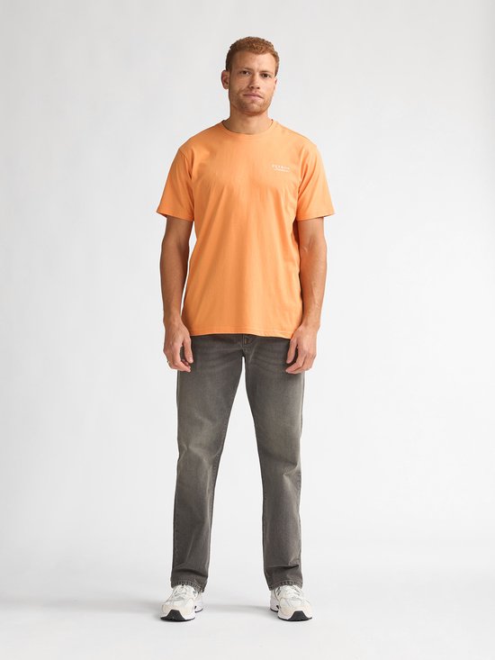 Man draagt een oranje t-shirt met "PETROL Industries" op de borst en een grijze jeans.