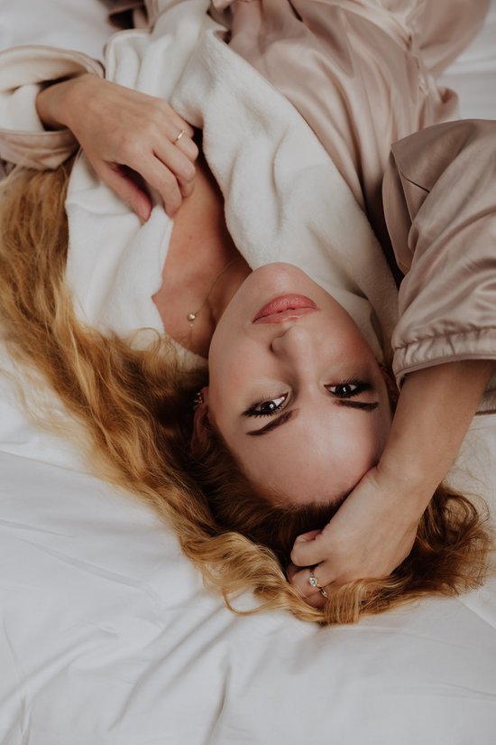 Vrouw met lang blond haar, liggend op een bed in satijnen badjas.