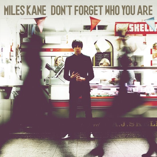 Miles Kane met 'Don't Forget Who You Are' albumhoes. Hij staat in een slagerij met bewegende figuren op de voorgrond.