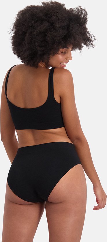 Model met krullend haar draagt een zwarte naadloze bralette en slip, bekeken vanaf de achterkant.