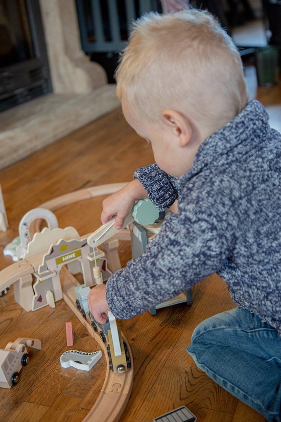 Jongen met blonde haren speelt met houten treinbaan. Hij duwt een trein door de mijn entree.