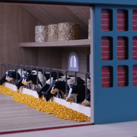 Speelgoedboerderij met zwart-wit koeien die eten uit een voerbak.