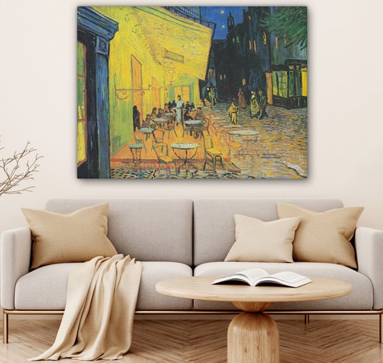 Een woonkamer met een bank en een schilderij van een terras 's avonds met een gele muur.