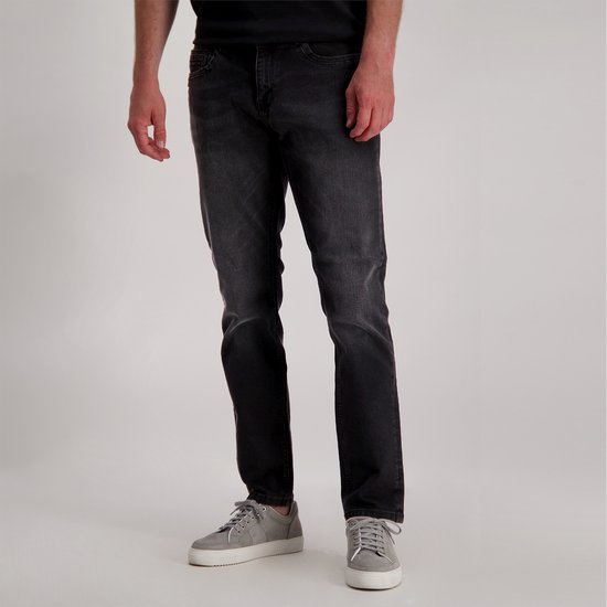 Man in een donkergrijze jeans, recht model, gedragen met grijze sneakers.
