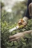 Handen knippen een groen lint met een Fiskars schaar met oranje handgrepen in een tuin.