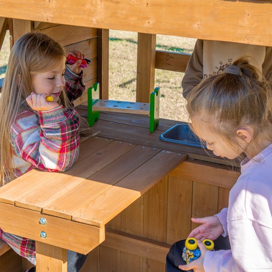 Twee jonge meisjes spelen aan een houten speelhuisje met een aanrecht en gootsteen.