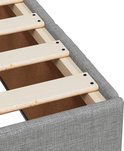 Gros plan du bord du boxspring gris clair avec sommier à lattes en bois.