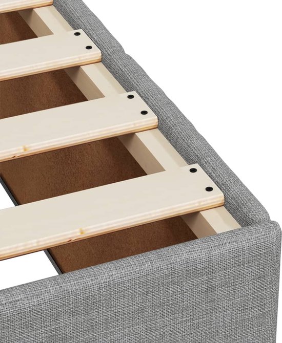 Gros plan du bord du boxspring gris clair avec sommier à lattes en bois.