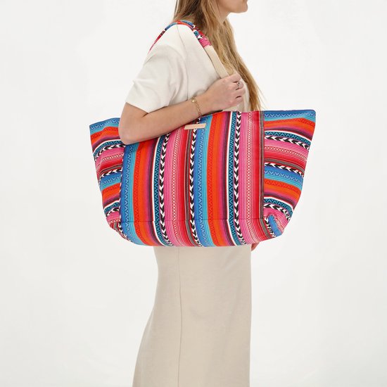 Model met beige jurk draagt grote tas met fuchsia, oranje en blauwe strepenprint.