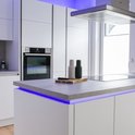 Moderne witte keuken met aanrecht, verlicht door een blauwe LED-strip.