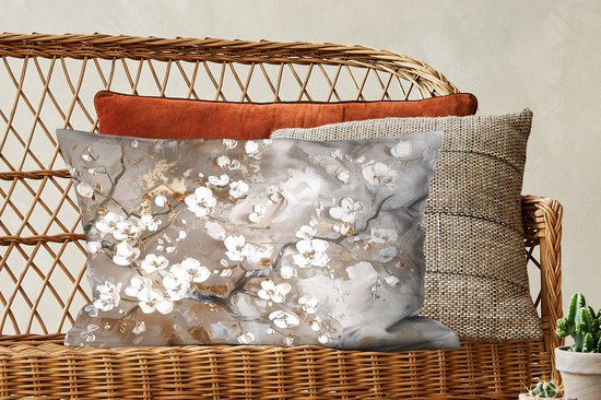 Coussin avec des branches de fleurs blanches et dorées sur une chaise en rotin avec d'autres coussins.