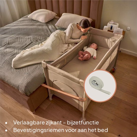 Zwart Lionelo reisbedje naast een bed, met een verlaagbare zijkant en bevestigingsriemen.