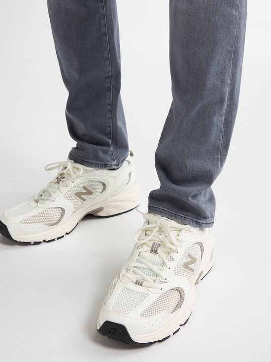 Detail van de voeten van een man in grijze jeans en witte 'New Balance' sneakers.