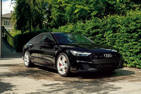 Zwarte Audi A7 sedan geparkeerd op een betegeld terras, met groene heggen op de achtergrond.