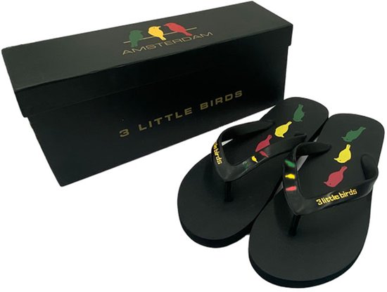 Zwarte teenslippers met de tekst '3 little birds' en vogels, naast een bijpassend zwart doosje met 'AMSTERDAM' en vogels.