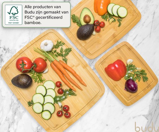 Drie bamboe snijplanken met 'budu' logo. Verse ingrediënten zoals tomaten, courgette, wortel, paprika, ui en knoflook liggen op de planken.