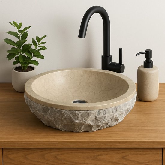 Bassin rond en marbre crème avec fond grossièrement taillé sur un plateau en bois, à côté d'un robinet noir et d'un distributeur de savon.