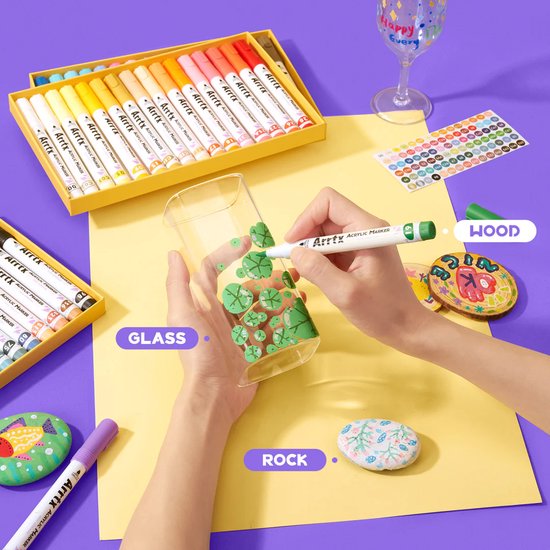 Arrtx acrylmarkers in gebruik op glas, met illustraties op steen, hout en een glas.