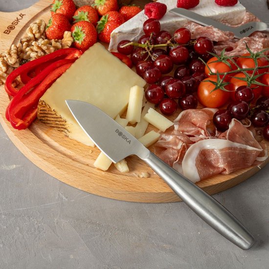 Planche de service en bois avec brie, fraises, framboises, raisins, tomates, morceaux de fromage et charcuterie, avec un couteau à fromage.