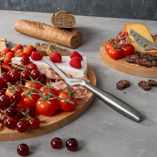 Gros plan d'une planche de service en bois avec brie, fraises, framboises, raisins, tomates et charcuterie.