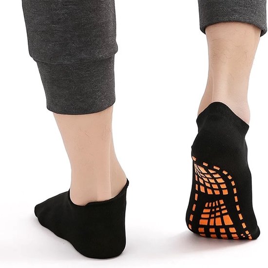 Zwarte enkelsokken met oranje antislip noppen op de zool, gedragen door een volwassene.