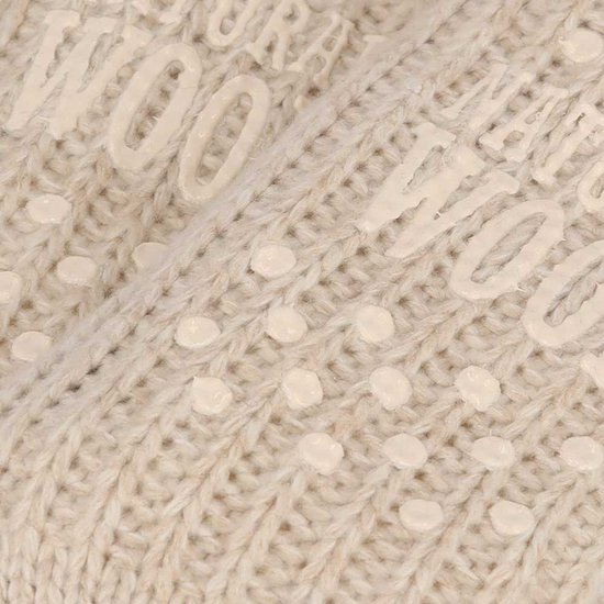 Detailopname van crème gebreide huissokken met op de zolen de tekst 'NATURAL WOOL' en antislip nopjes.