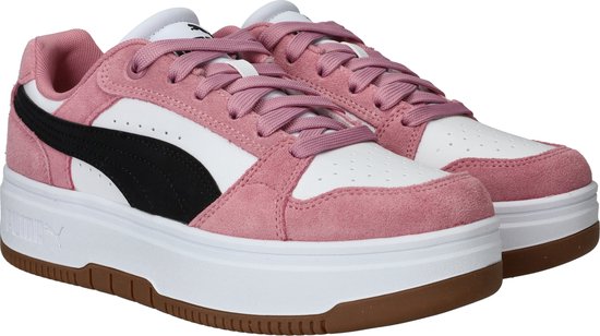Twee roze suède Puma sneakers met witte en zwarte accenten, op een witte plateauzool.