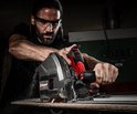 Man met veiligheidsbril gebruikt de Einhell invalzaag op een houten plank, met rondvliegend zaagsel.