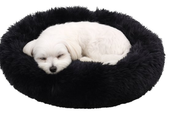 Un petit chien blanc dort enroulé dans un coussin rond, noir et ultra-doux pour chien.