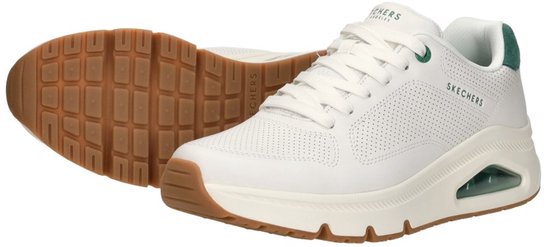 Witte Skechers sneakers met groene hiel en bruine zool, één schoen ligt op de zool.