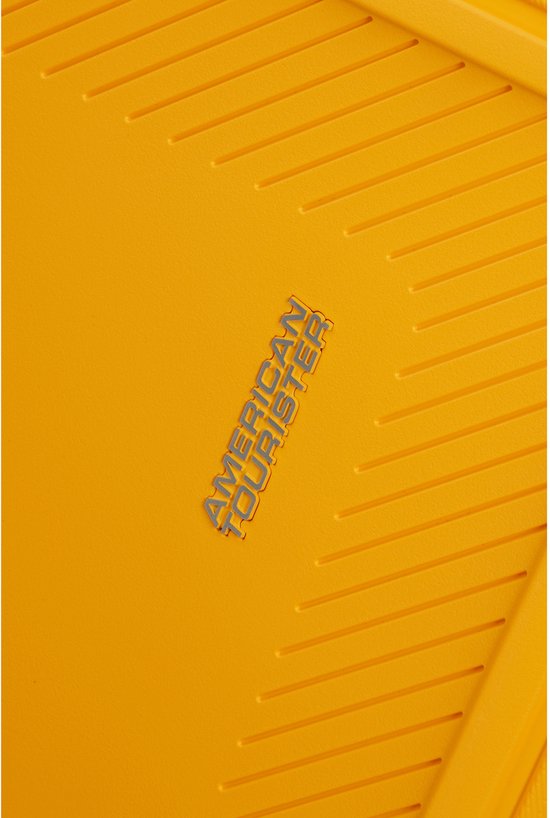Detail van gouden gele koffer met "AMERICAN TOURISTER" logo en ribbelpatroon.