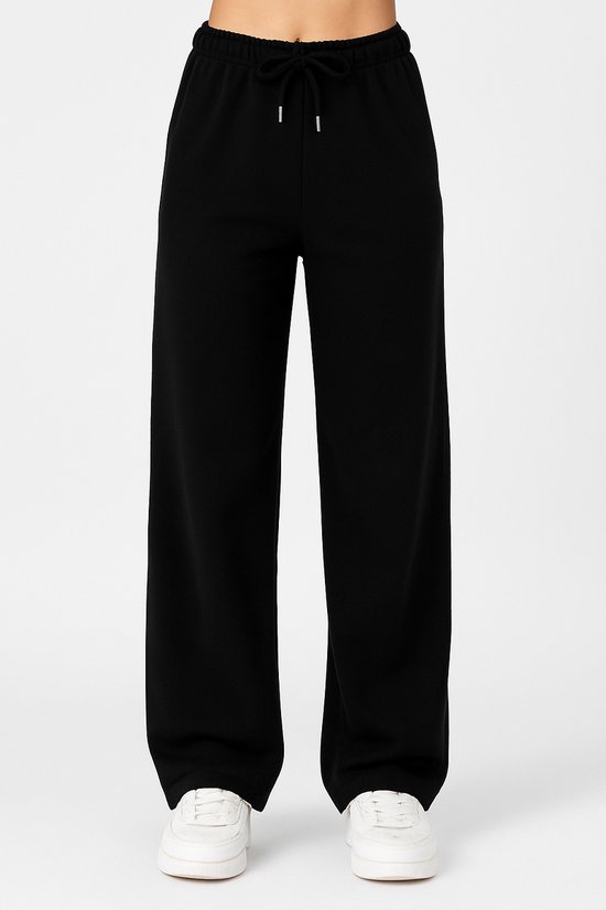 Vooraanzicht van een zwarte wijde joggingbroek met trekkoord en witte sneakers.