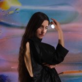 Vrouw met lang bruin haar in een zwarte outfit, vasthoudend een glimmend object in haar hand tegen een abstracte achtergrond.