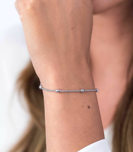 Zilverkleurige armband met een fijne ketting en vier bolletjes, gedragen op een arm.