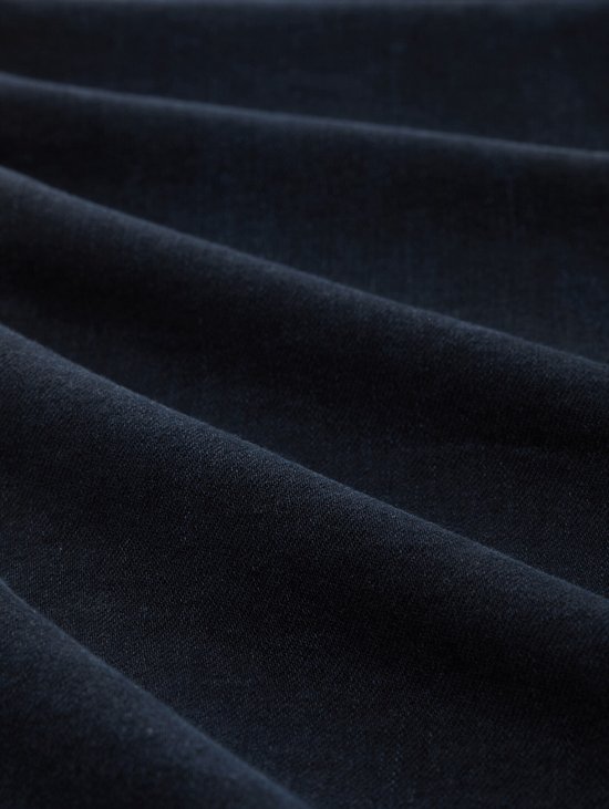 Close-up van de textuur van donkerblauwe denim stof met golvende plooien.