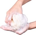 Een spons van loofah en badstof wordt in schuimende handen gebruikt.