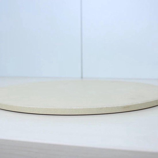 Ronde, beige pizzasteen met subtiele textuur, gefotografeerd op een lichte ondergrond.