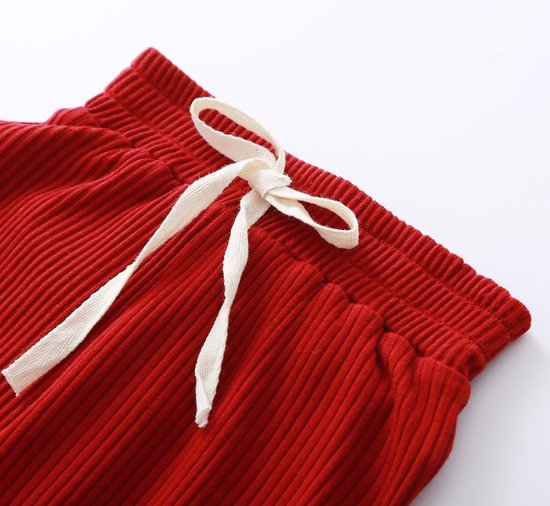 De tailleband van een rode, geribbelde broek met een witte strik.