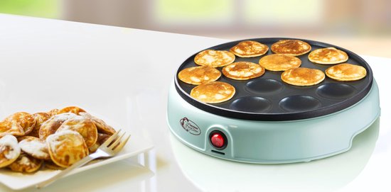 Lichtgroene poffertjespan met 12 goudbruine poffertjes, naast een bord met poedersuiker bestoven poffertjes.